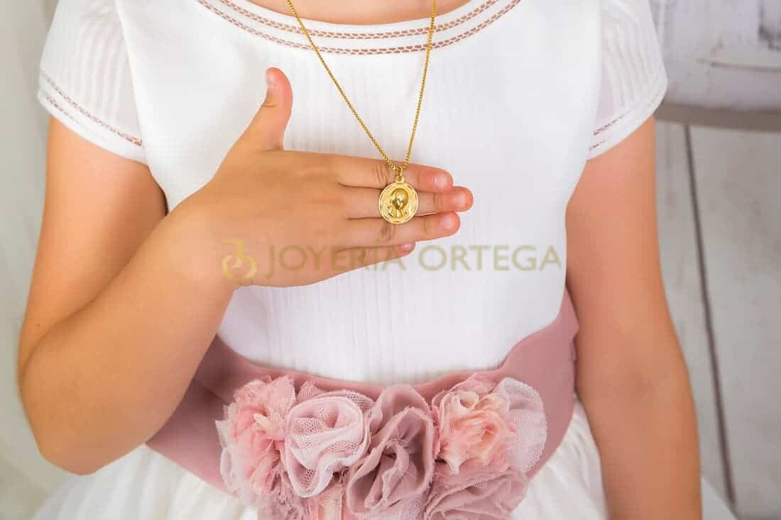 Niña sostiene medallón dorado, ropa blanca y rosa